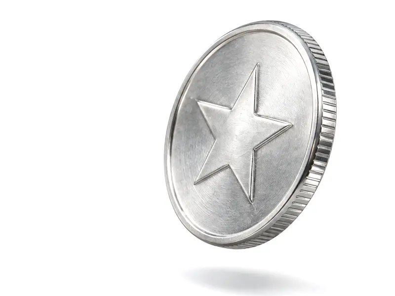 A silver-coloured coin with a star in relief, tilted in mid-air above its shadow on a white surface