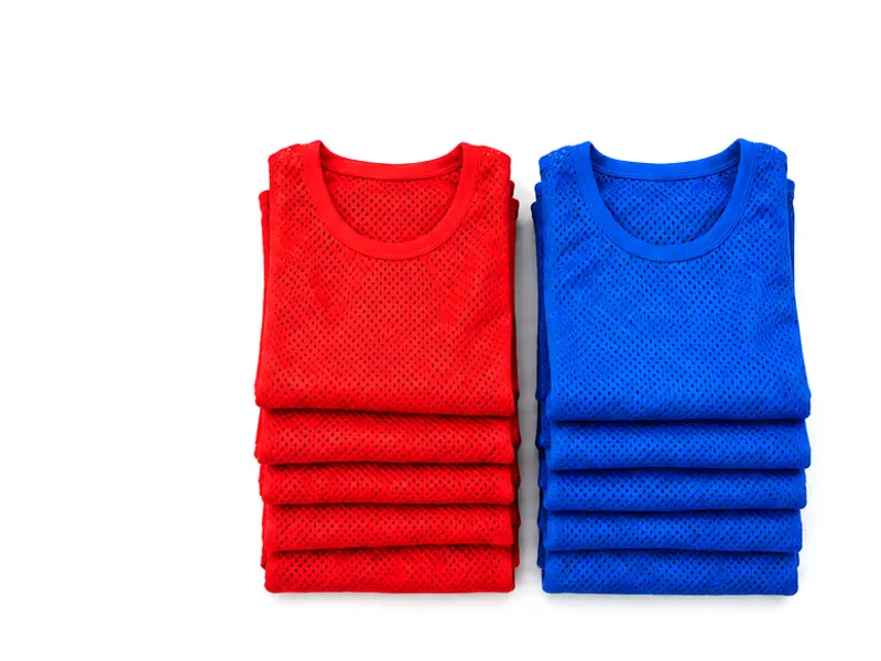 Two piles of folded training bibs, one red and one blue, on a white surface